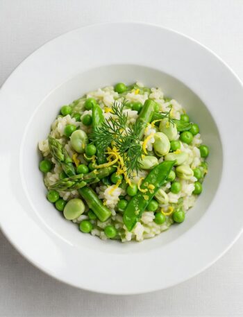 Creamy risotto with green asparagus and peas, topped with fresh herbs in a white ceramic bow
